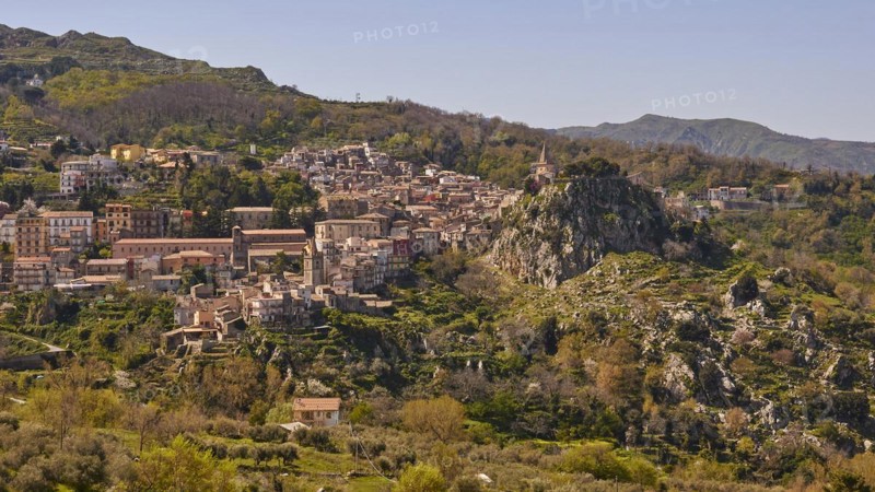 View of a town in the middle of a mountainous landscape with dense vegetation. Novara di Sicilia, Sicily, Italy, Europe
