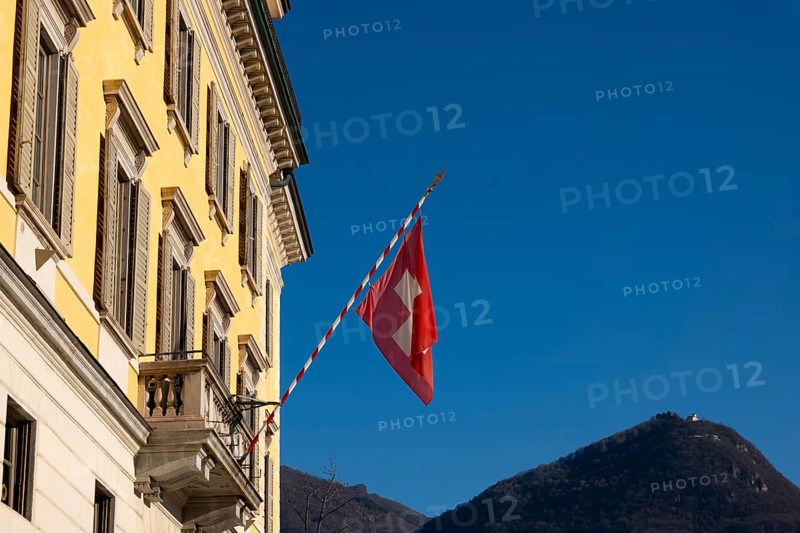 Swiss Flag on City Hall and Mountain Peak Monte Bre Against Blue Clear Sky in a Sunny Day in Lugano, Ticino, Switzerland, Europe