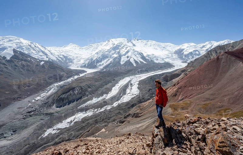 Mountaineer at Traveller's Pass with view of impressive mountain landscape, high mountain landscape with glacier moraines and glacier tongues, glaciated and snow-covered mountain peaks, Lenin Peak and Peak of the XIX Party Congress of the CPSU, Trans Alay Mountains, Pamir Mountains, Osh Province, Kyrgyzstan, Asia