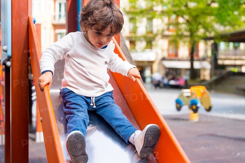 A small girl sliding down a slide in an urban playground