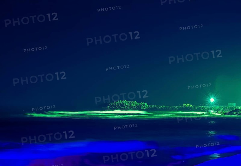 Night scene of ocean pier with single street light taken with long shutter speed creating blue color cast of nearby waves