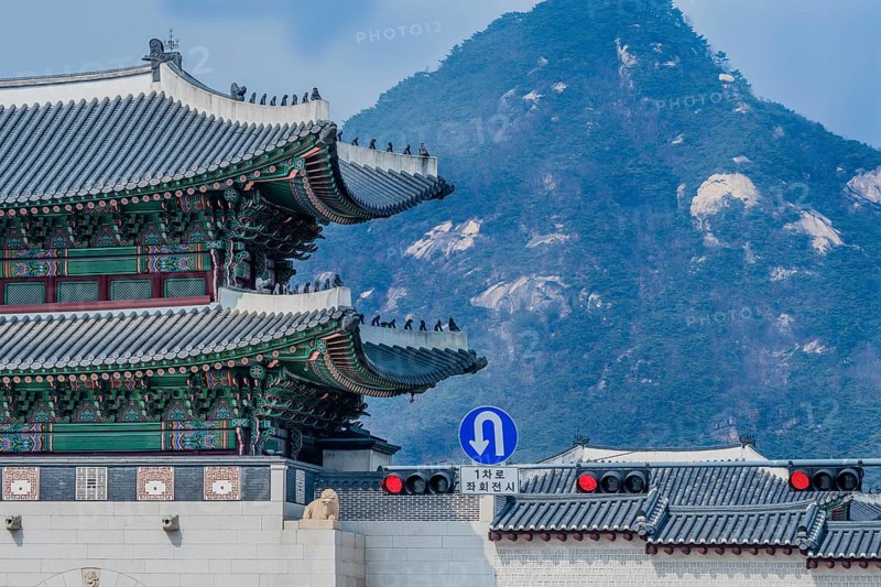 Seoul, South Korea, March 18, 2017:Tiled roof of Seoul's Gyeong Bok Gung Palace in stunning colors with a traffic light and sign that says one lane left u-turn in Korean language and a mountain in the background, Asia