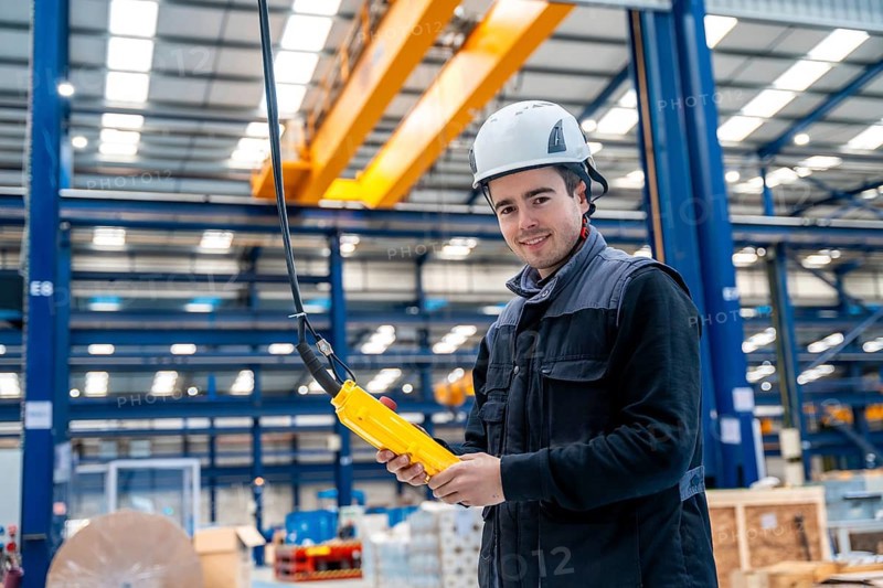Engineer with protective hard hat controlling an industrial crane with control remote