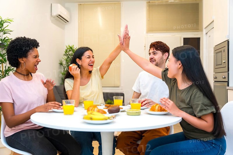 Multi-ethnic friends celebrating while high-fiving during breakfast together at home