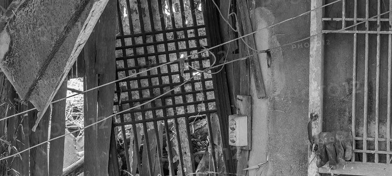 Black and white of interior of abandoned shack with wood lattice windows and an old electrical outlet attached to a piece of wood