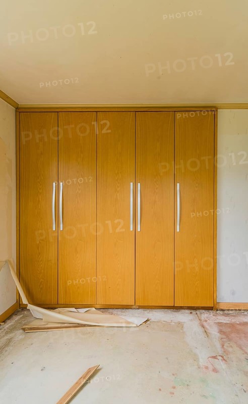 Wooden doors with metal handles of built-in closets in bedroom with debris and trash on floor in abandoned house