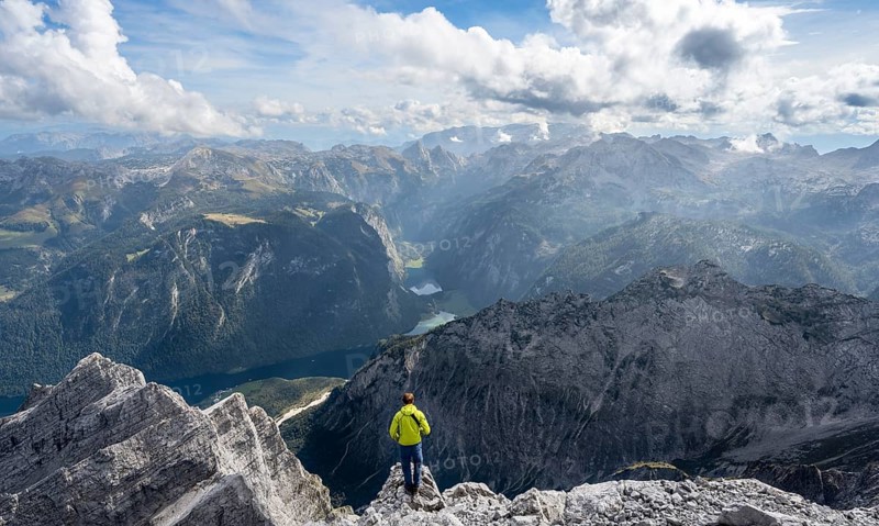 Mountaineer on the rocky summit of the Watzmann Mittelspitze, Watzmann crossing, view of mountain panorama with Steinernes Meer and Koenigssee, Berchtesgaden National Park, Berchtesgaden Alps, Bavaria, Germany, Europe