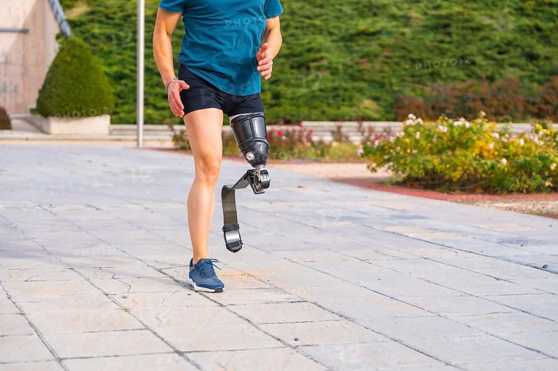 Lower part of a runner with prosthetic leg running along a park