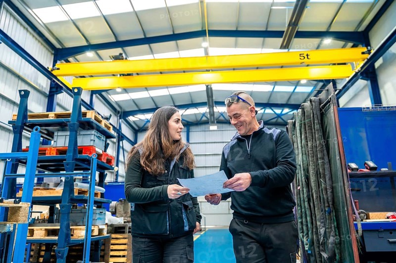 Teamwork of engineers talking and looking at a paper while working in a cnc logistics factory