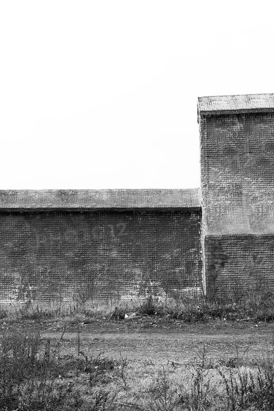 Black and white of small wire-frame and stucco building in countryside. Building has no window or doors