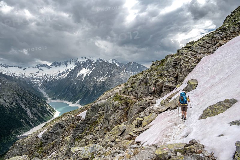 Mountaineer on hiking trail with snow, view of Schlegeisspeicher, glaciated rocky mountain peaks Hoher Weisszint and Hochfeiler with glacier Schlegeiskees, Berliner Hoehenweg, Zillertal Alps, Tyrol, Austria, Europe
