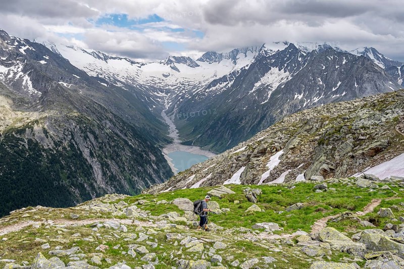 Mountaineer on hiking trail, view of Schlegeisspeicher, glaciated rocky mountain peaks Hoher Weisszint and Hochfeiler with glacier Schlegeiskees, Berliner Hoehenweg, Zillertal Alps, Tyrol, Austria, Europe