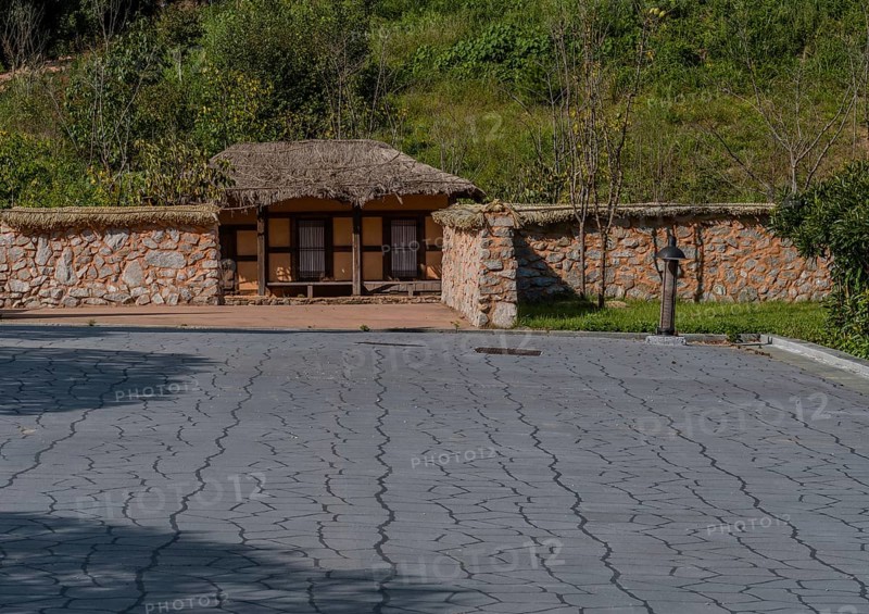 Old thatch roof building behind mud and stone wall at urban public park