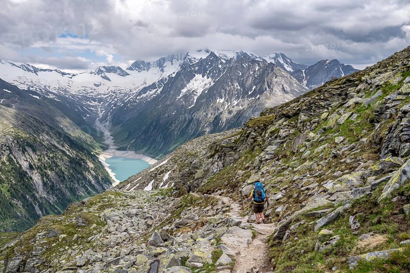 Mountaineer on hiking trail, view of Schlegeisspeicher, glaciated rocky mountain peaks Hoher Weisszint and Hochfeiler with glacier Schlegeiskees, Berliner Hoehenweg, Zillertal Alps, Tyrol, Austria, Europe