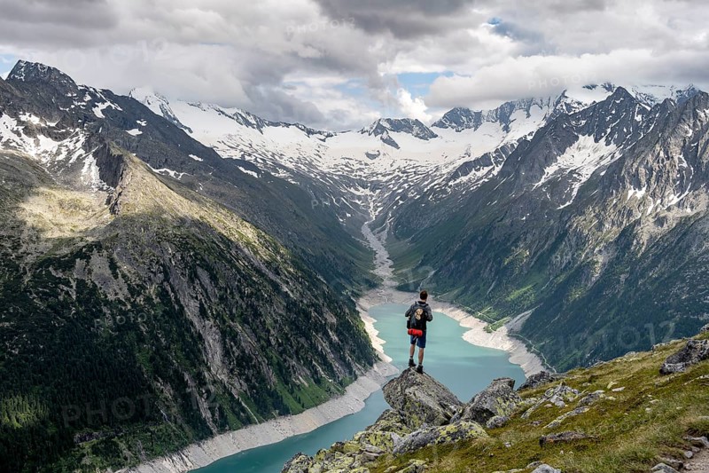 Mountaineer on a rock in front of a mountain panorama, view of Schlegeisspeicher, glaciated rocky mountain peaks Hoher Weisszint and Hochfeiler with glacier Schlegeiskees, Berliner Hoehenweg, Zillertal Alps, Tyrol, Austria, Europe