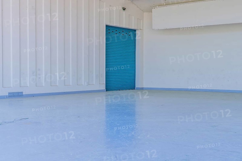 Large blue metal door in white wall reflecting onto concrete floor of amphitheater in urban public park