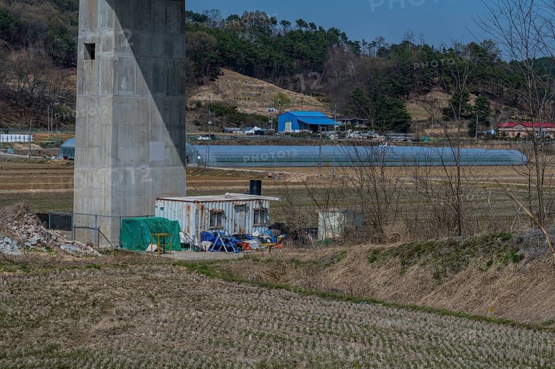 White metal storage building surrounded by debris beside concrete bridge support column