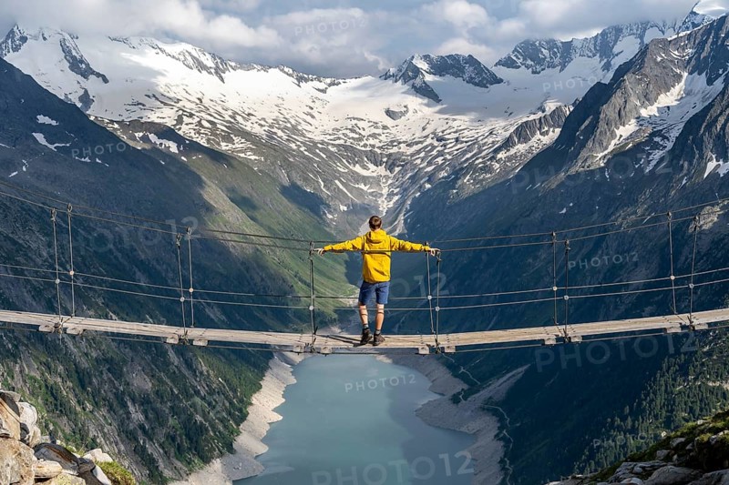 Mountaineers on a suspension bridge, picturesque mountain landscape near the Olpererhuette, view of turquoise-blue lake Schlegeisspeicher, glaciated rocky mountain peaks Hoher Weisszint and Hochfeiler with glacier Schlegeiskees, Berliner Hoehenweg, Zillertal Alps, Tyrol, Austria, Europe