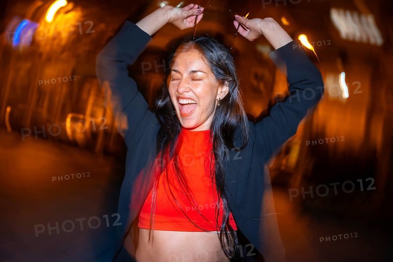 Night photo with flash and motion of an excited woman dancing alone in the city street