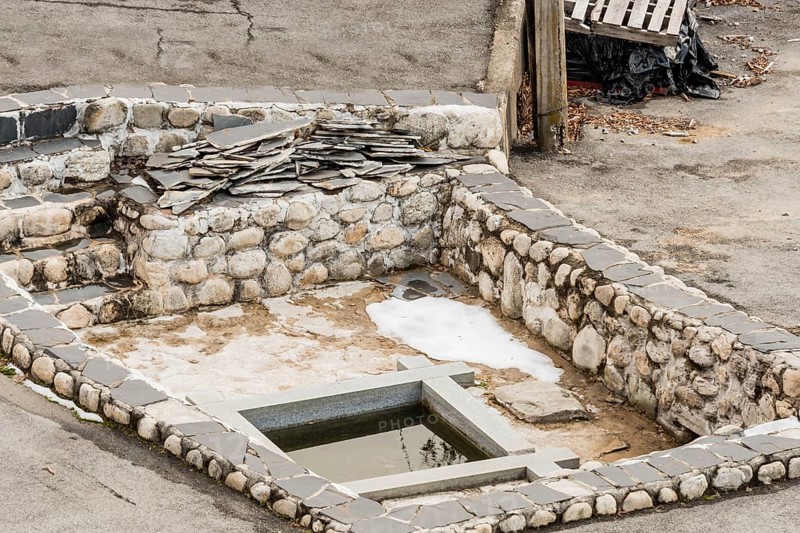 Remains of building foundation made of stone and concrete with square pool of water in center