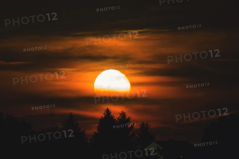 An atmospheric moonrise with orange glowing clouds and tree silhouettes, Haan, North Rhine-Westphalia, Germany, Europe