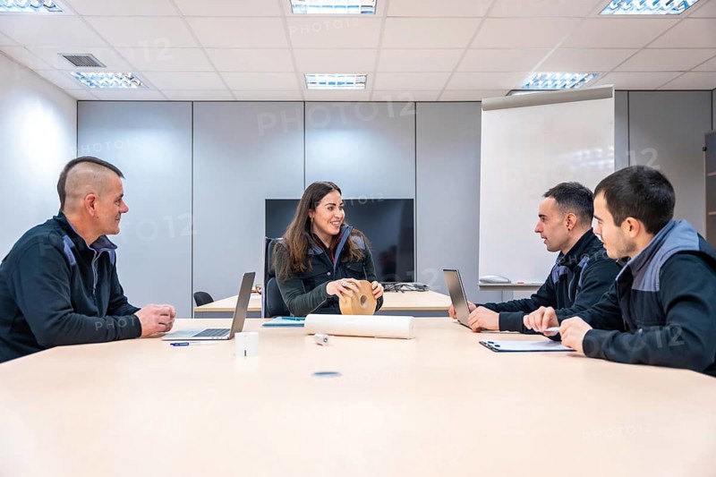Manager leading a meeting with engineers in a factory room with table and board
