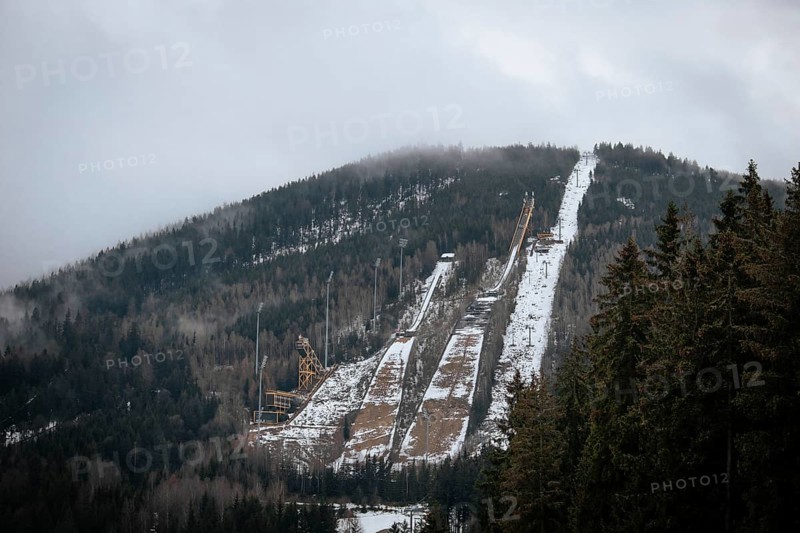 A ski jump tower stands on a snowy mountain slope with cloudy skies above, czech harrachov