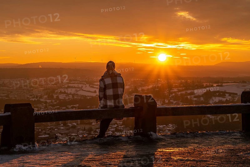 Person sitting on a wooden railing looking at the sunset over a wintry landscape, Wallberg, Pforzheim, Germany, Europe