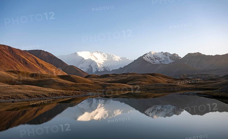 White glaciated and snowy mountain peak Pik Lenin at sunset, mountains reflected in a lake between golden hills, Trans Alay Mountains, Pamir Mountains, Osh Province, Kyrgyzstan, Asia