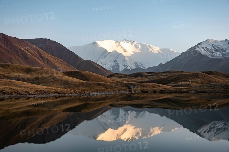 White glaciated and snowy mountain peak Pik Lenin at sunset, mountains reflected in a lake between golden hills, Trans Alay Mountains, Pamir Mountains, Osh Province, Kyrgyzstan, Asia