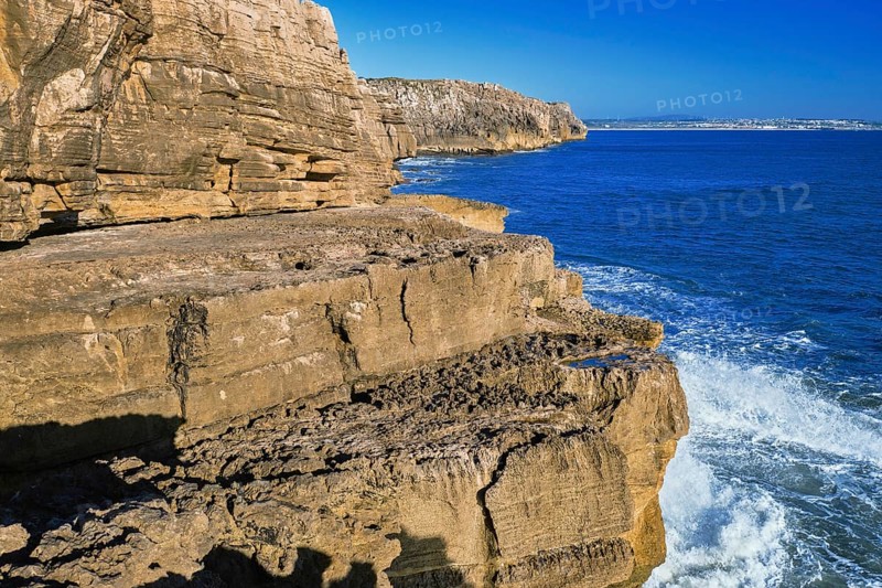 Beautiful cliffs and rock formations in Peniche, Portugal, on sunny day. Weathered rock formations, geological interest, cliffs, blue sea waves, tide, coastline, clear blue sky, Europe