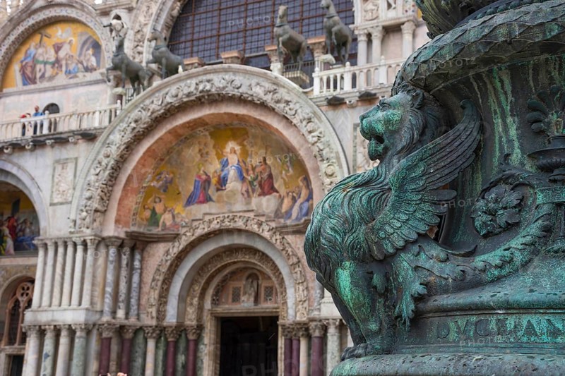 Old street ornament with winged lions and San Marco Basilica in the background, in St. Mark Square, famous tourist attraction in Venice, Italy. Selective focus