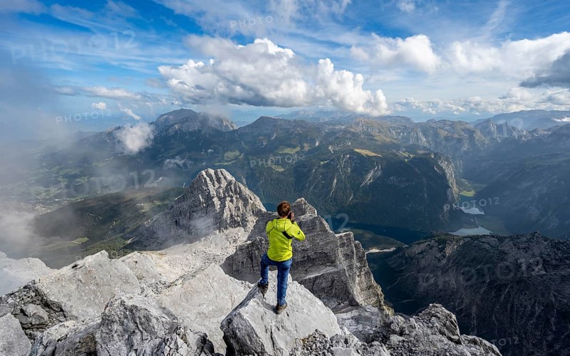 Mountaineer on the rocky summit of the Watzmann Mittelspitze, Watzmann crossing, view of mountain panorama with Steinernes Meer and Koenigssee, Kleiner Watzmann and Watzmann children, Berchtesgaden National Park, Berchtesgaden Alps, Bavaria, Germany, Europe