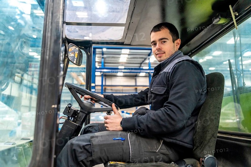 Male manual worker driving a forklift in a modern cnc logistic factory