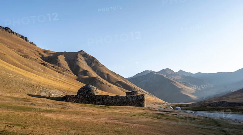 Historic caravanserai Tash Rabat from the 15th century, in the evening light with golden hills and yurts, Naryn region, Kyrgyzstan, Asia