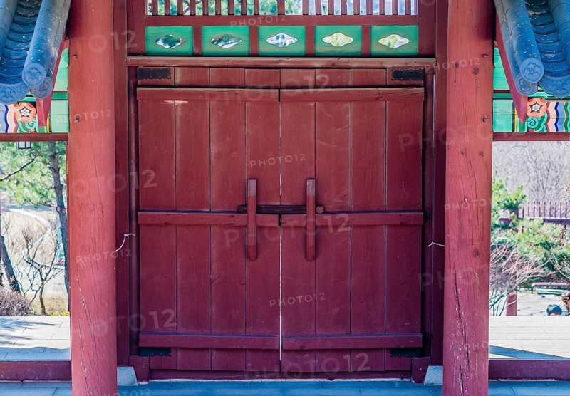 Red wooded gate with tiled roof and colorful, oriental design at a local woodland park in South Korea