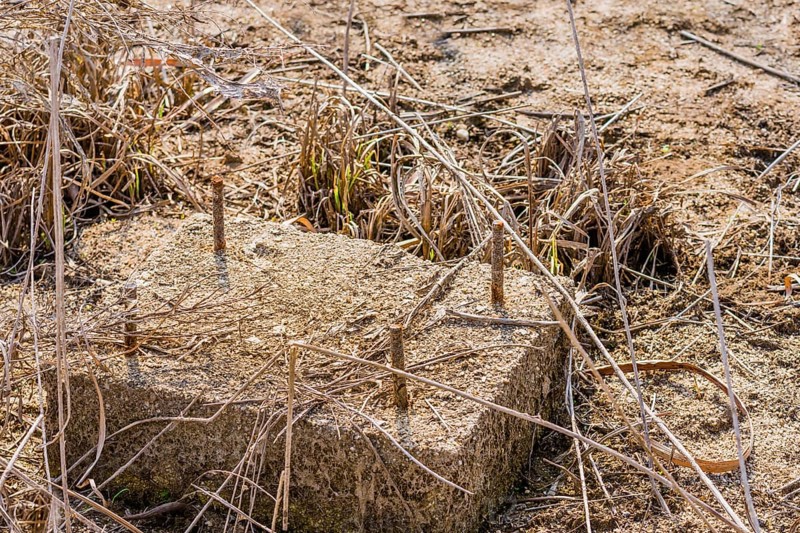 Concrete block with threaded metal bars that is part of building foundation in tall grass of dried riverbed