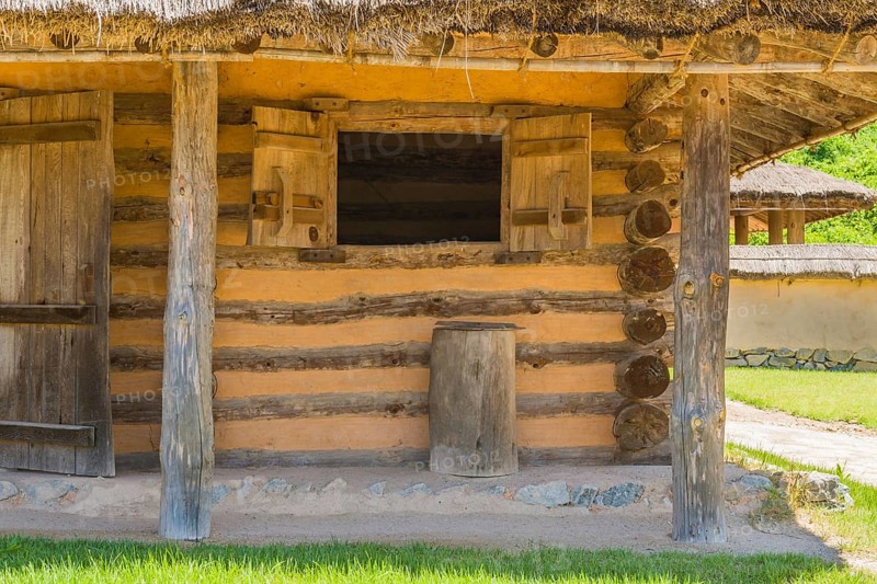 Exterior of log cabin with concrete and stone porch and thatch covered roof