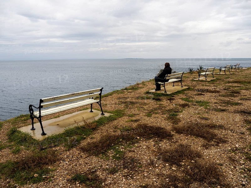 Tourist sitting on a bench and looking out to sea, near Veli Losinj, Kvarner Bay, Croatia, Europe
