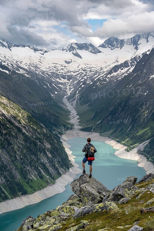 Mountaineer on a rock in front of a mountain panorama, view of Schlegeisspeicher, glaciated rocky mountain peaks Hoher Weisszint and Hochfeiler with glacier Schlegeiskees, Berliner Hoehenweg, Zillertal Alps, Tyrol, Austria, Europe