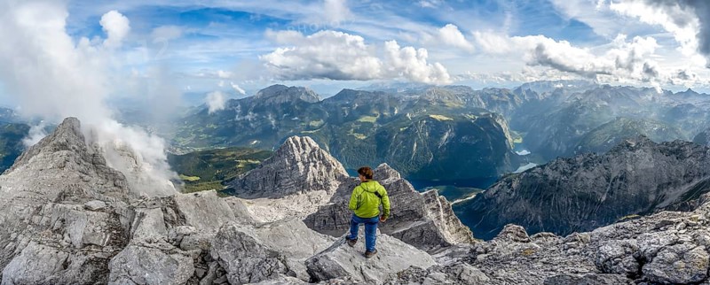 Mountaineer on the rocky summit of the Watzmann Mittelspitze, Watzmann crossing, view of mountain panorama with Steinernes Meer and Koenigssee, Berchtesgaden National Park, Berchtesgaden Alps, Bavaria, Germany, Europe
