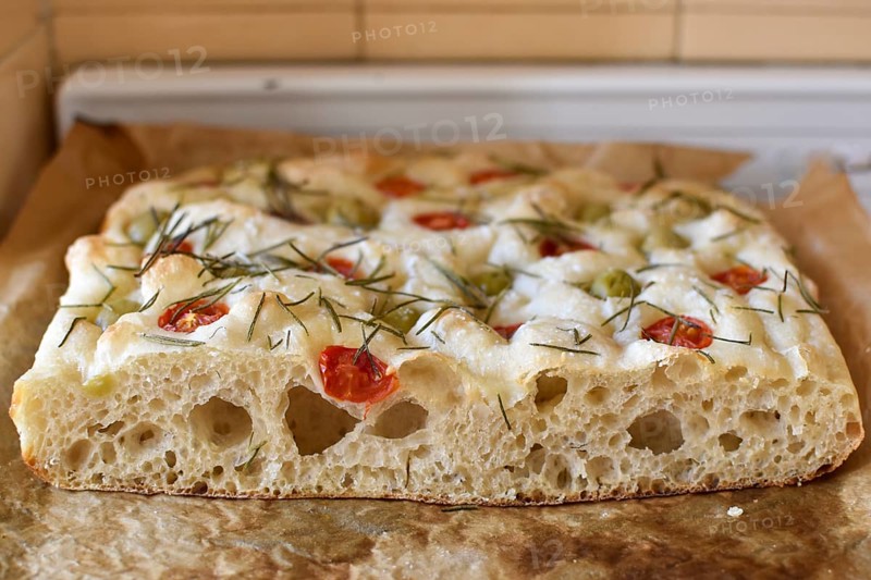 Homemade Italian flatbread focaccia with cherry tomatoes, olives and rosemary in a rustic kitchen