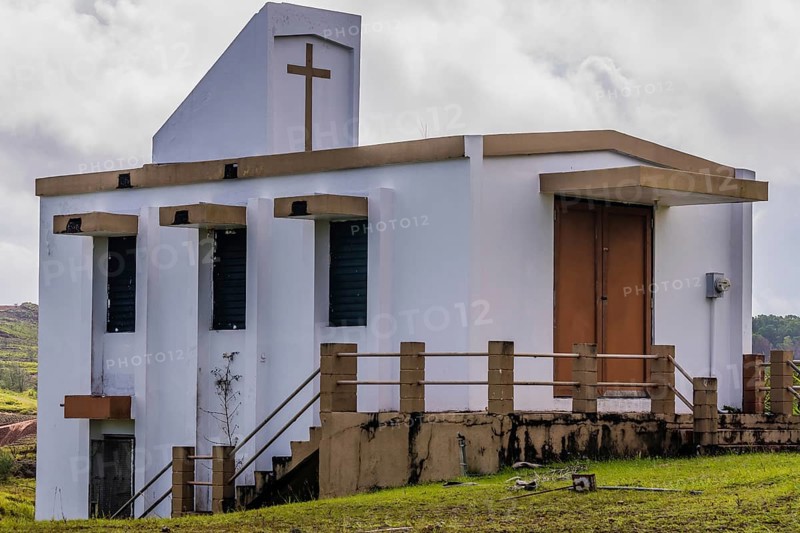Side view of a small white country church sitting on a hillside in Guam with cloudy sky in the background