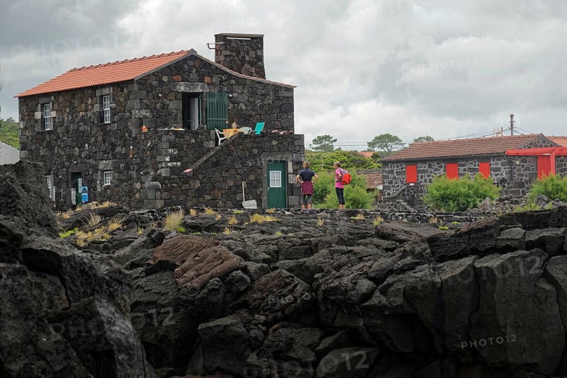 People standing next to a stone house on lava rock under an overcast sky, North Coast, Santa Luzia, Pico, Azores, Portugal, Europe