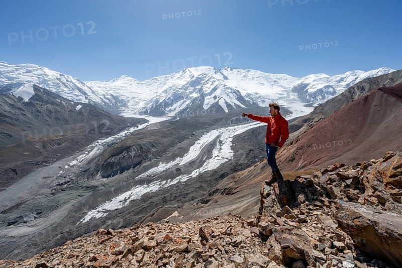 Mountaineer points into the distance, at Traveller's Pass with view of impressive mountain landscape, high mountain landscape with glacier moraines and glacier tongues, glaciated and snow-covered mountain peaks, Lenin Peak and Peak of the XIX Party Congress of the CPSU, Trans Alay Mountains, Pamir Mountains, Osh Province, Kyrgyzstan, Asia