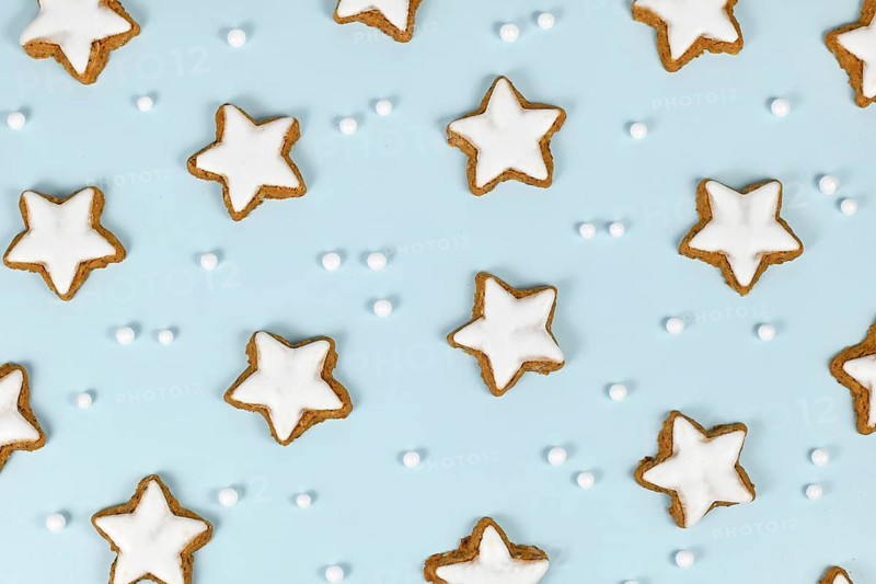 Top view of German star shaped glazed cinnamon Christmas cookies called 'Zimtsterne' on light blue background with snowball ornaments