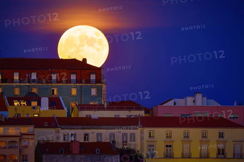 Beautiful view of big full moon rising behind a row of old houses in European city, Lisbon, Portugal. Supermoon, close up, Europe, night, landscape, cityscape, clear sky. Romantic evening, fairy tales, stories