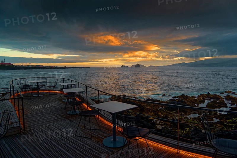 Terrace of the Cella Bar overlooking the coast of Madalena and the distant island of Faial at sunset under dramatic clouds, Madalena, Pico, Azores, Portugal, Europe