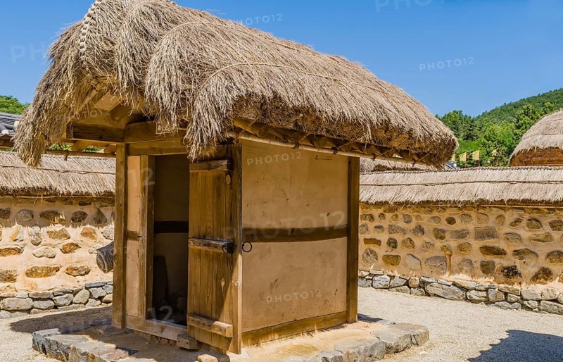 Buyeo, South Korea, July 7, 2018: Traditional outhouse with straw thatch roof and wooden door inside a mud and stone wall in public park at Neungsa Baekje Temple. For editorial use only, Asia