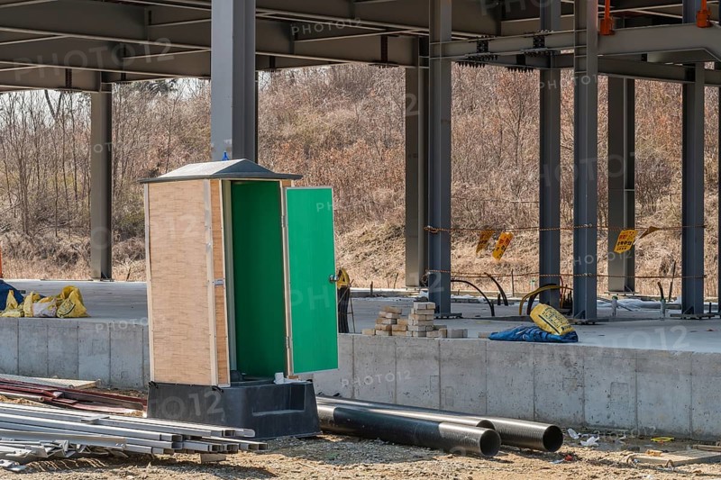 Chungju, South Korea, March 22, 2020: For editorial use only. Port-a-potty with open door at construction site next to unfinished industrial building, Asia